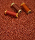Case Bouclé fabric in terracotta styled with coordinating red, rust and orange thread spools, showcasing the textured bouclé weave and warm colour variations.