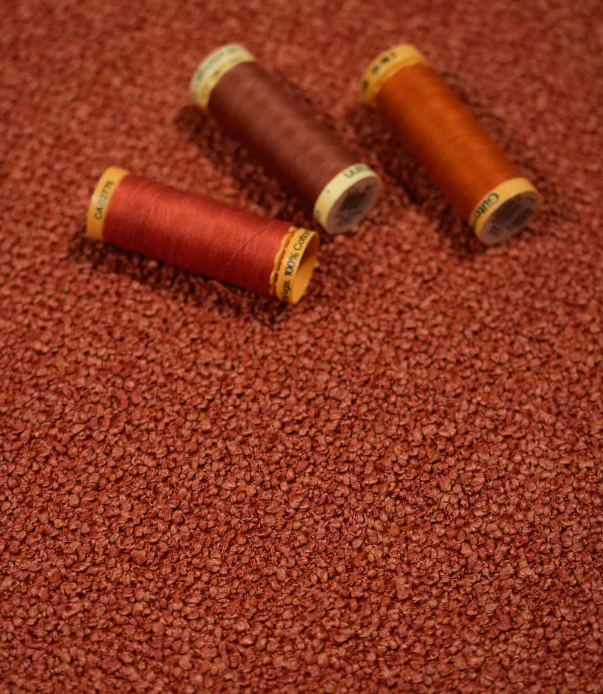 Case Bouclé fabric in terracotta styled with coordinating red, rust and orange thread spools, showcasing the textured bouclé weave and warm colour variations.