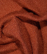 Case Bouclé terracotta upholstery fabric loosely draped into folds, highlighting its tactile bouclé texture, flexibility and rich rust-orange colour.