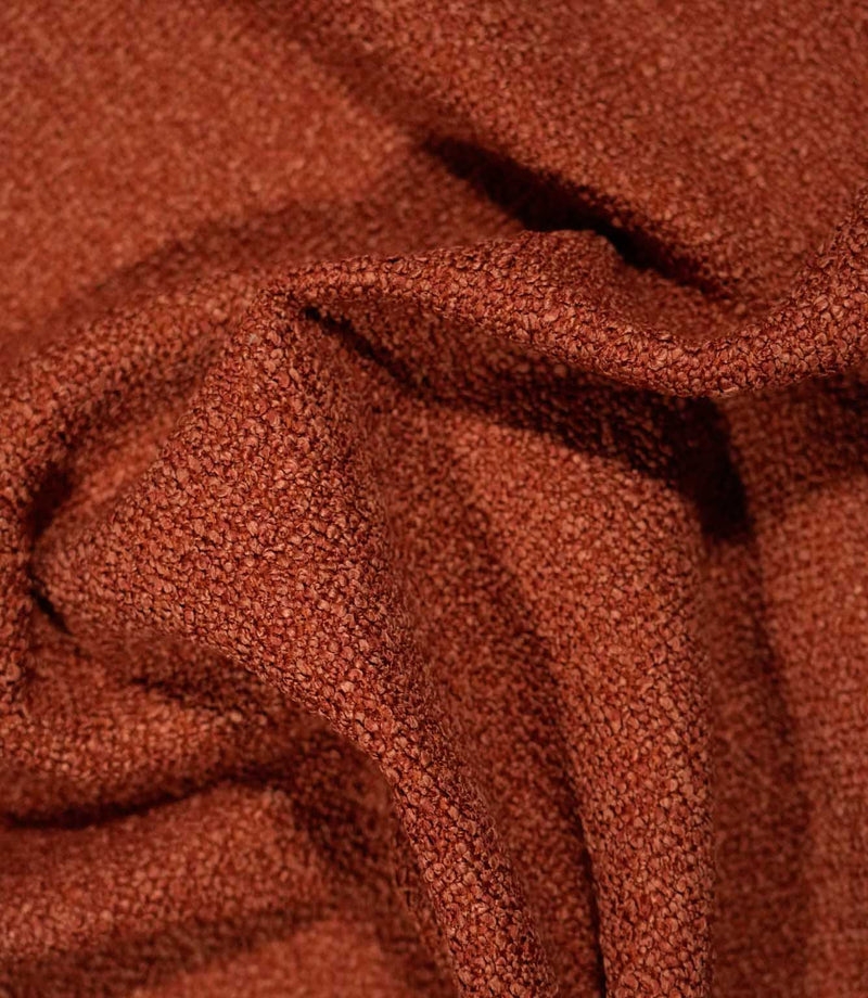 Case Bouclé terracotta upholstery fabric loosely draped into folds, highlighting its tactile bouclé texture, flexibility and rich rust-orange colour.