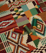 Multicoloured geometric upholstery fabric laid flat with coordinating thread spools, highlighting the bold Southwestern patchwork design and woven texture.