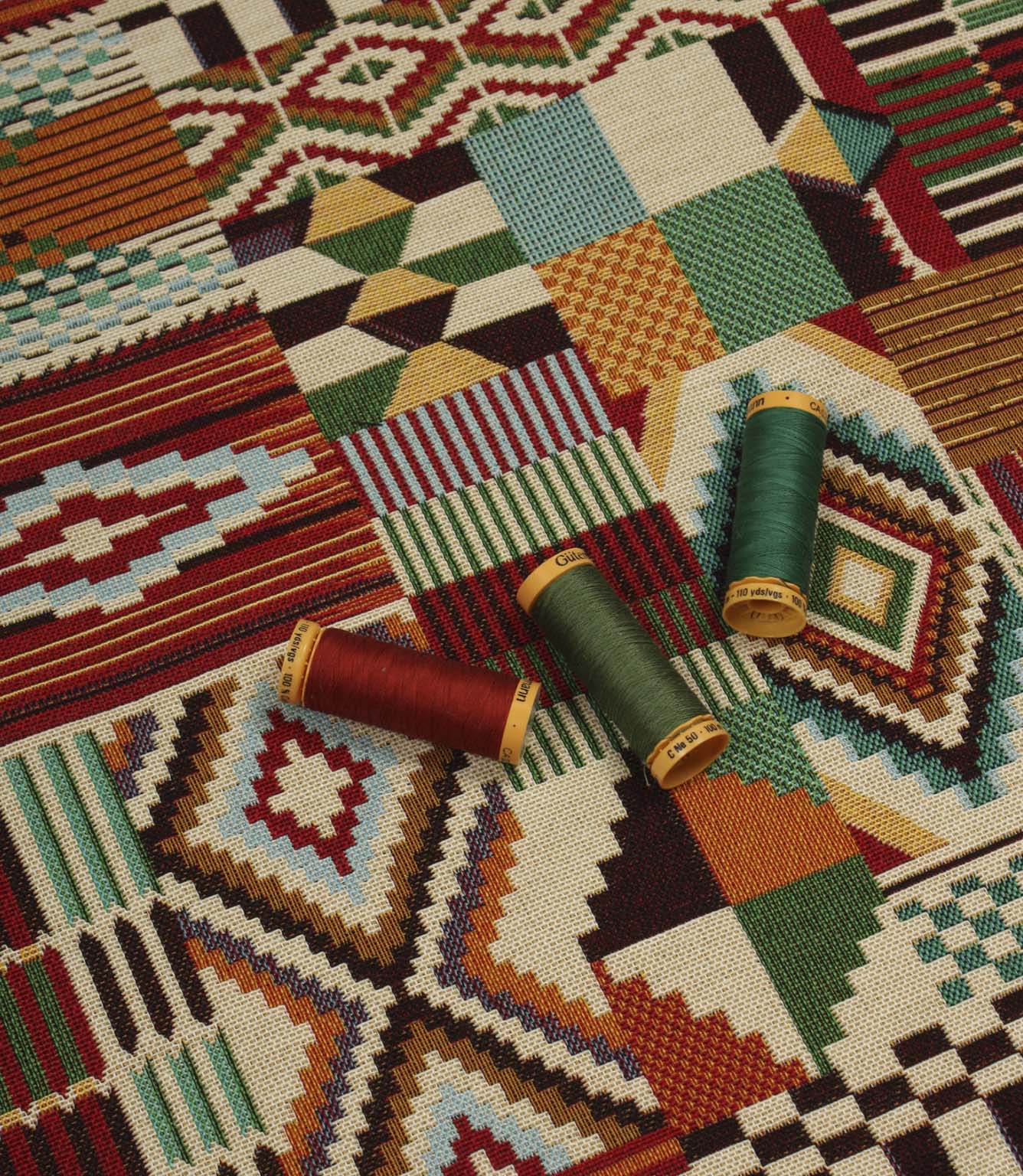 Multicoloured geometric upholstery fabric laid flat with coordinating thread spools, highlighting the bold Southwestern patchwork design and woven texture.