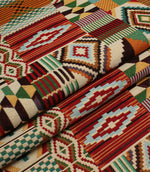 Folded Southwestern-style fabric displaying the structured drape and colourful geometric tapestry pattern in rich red, teal, ochre, and cream shades.