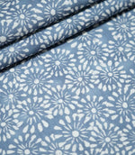 Close-up of Chamberry Bluebell floral fabric arranged in overlapping folds, highlighting the repeating white daisy-like flowers, soft blue background and finely textured weave.