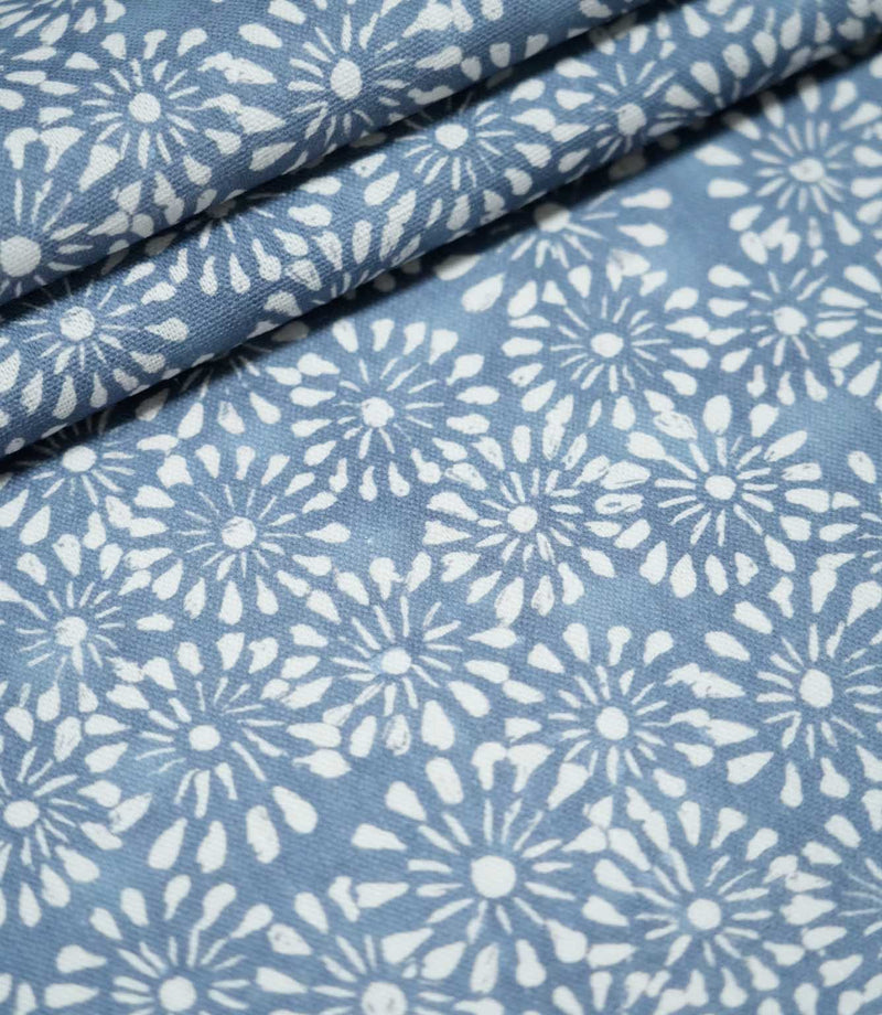 Close-up of Chamberry Bluebell floral fabric arranged in overlapping folds, highlighting the repeating white daisy-like flowers, soft blue background and finely textured weave.