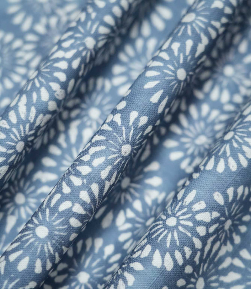 Chamberry Bluebell floral fabric gathered into soft, flowing folds, displaying the repeating white daisy-inspired motifs on a dusty blue background and showing how the printed pattern follows the fabric's drape.