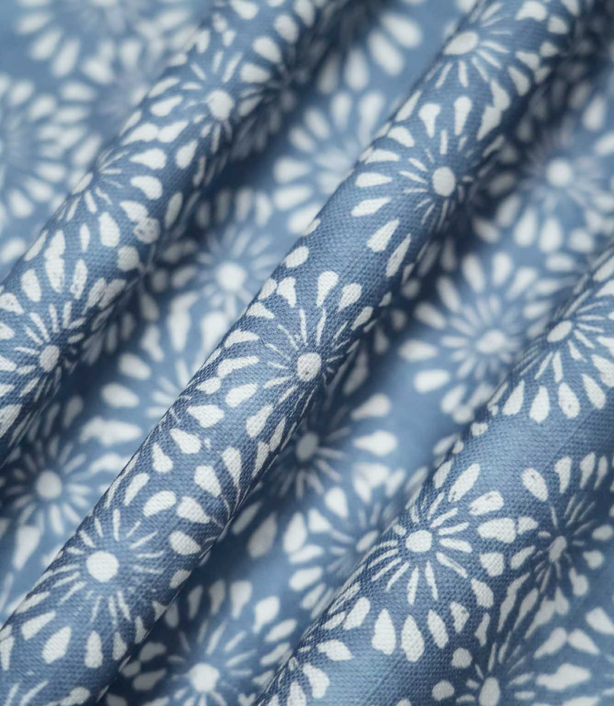 Chamberry Bluebell floral fabric gathered into soft, flowing folds, displaying the repeating white daisy-inspired motifs on a dusty blue background and showing how the printed pattern follows the fabric's drape.