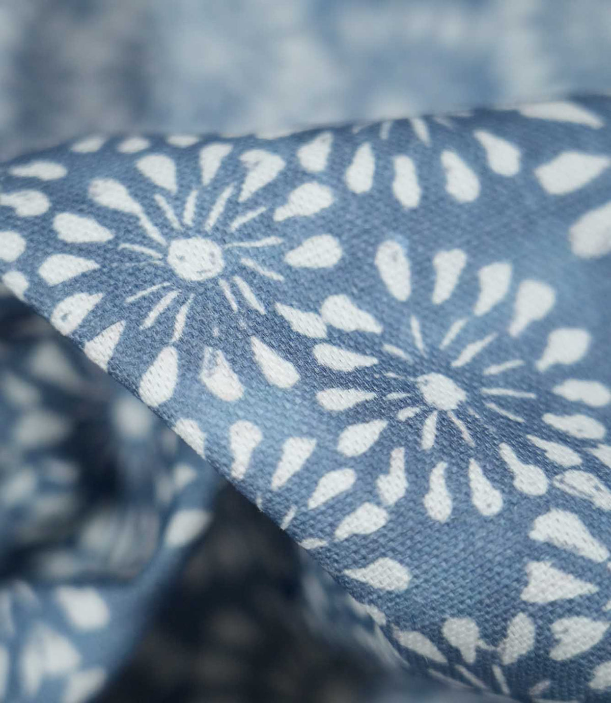 Macro photograph of Chamberry Bluebell fabric showing the fine woven texture and detailed white floral motifs, with rounded petals and delicate radiating lines printed onto a soft blue background.