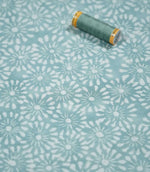 Chamberry Duck Egg fabric photographed with a coordinating sewing thread spool for scale, highlighting the small white floral motifs, soft duck egg colour and subtly textured woven surface.