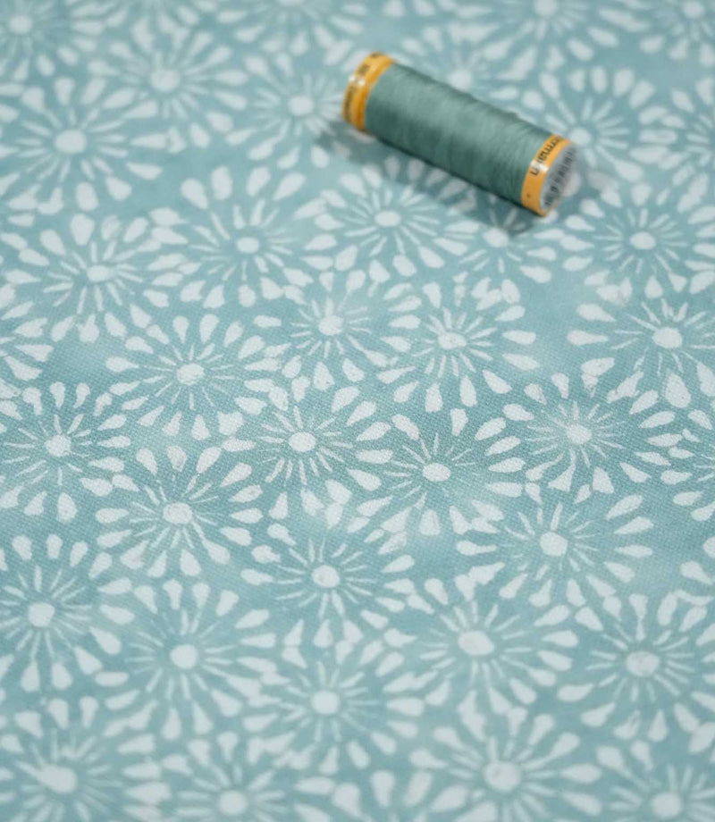 Chamberry Duck Egg fabric photographed with a coordinating sewing thread spool for scale, highlighting the small white floral motifs, soft duck egg colour and subtly textured woven surface.
