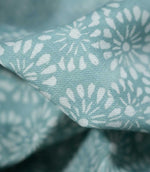 Macro photograph of Chamberry Duck Egg fabric showing the fine woven texture, soft duck egg blue-green background and delicate white floral motifs with rounded petals and fine radiating lines.