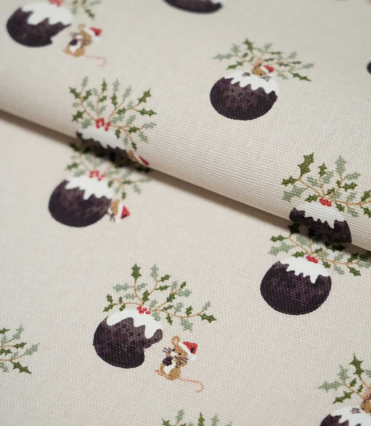Folded Christmas Pudding Neutral fabric displaying the repeating Christmas pudding design with green holly, red berries and small mice wearing red festive hats.