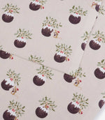 A close-up of patterned fabric showing a repeating print of Christmas puddings, holly leaves, mistletoe, and small mice on a light warm beige background.
