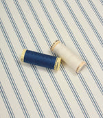 Classic striped fabric shown with navy blue and ivory thread spools against a delicate blue ticking stripe pattern.