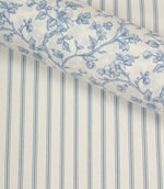 Coordinating blue floral fabric layered over a traditional blue ticking stripe fabric with an ivory background and fine vertical lines.