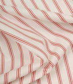 Softly folded ivory fabric with red ticking stripes, showing the gentle drape and lightweight woven texture.