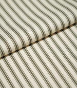 Folded JF Ticking Forest fabric showing its classic narrow forest green ticking stripe pattern on a warm ivory textured ground.