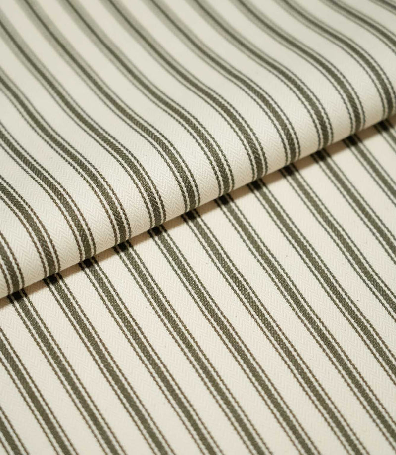 Folded JF Ticking Forest fabric showing its classic narrow forest green ticking stripe pattern on a warm ivory textured ground.