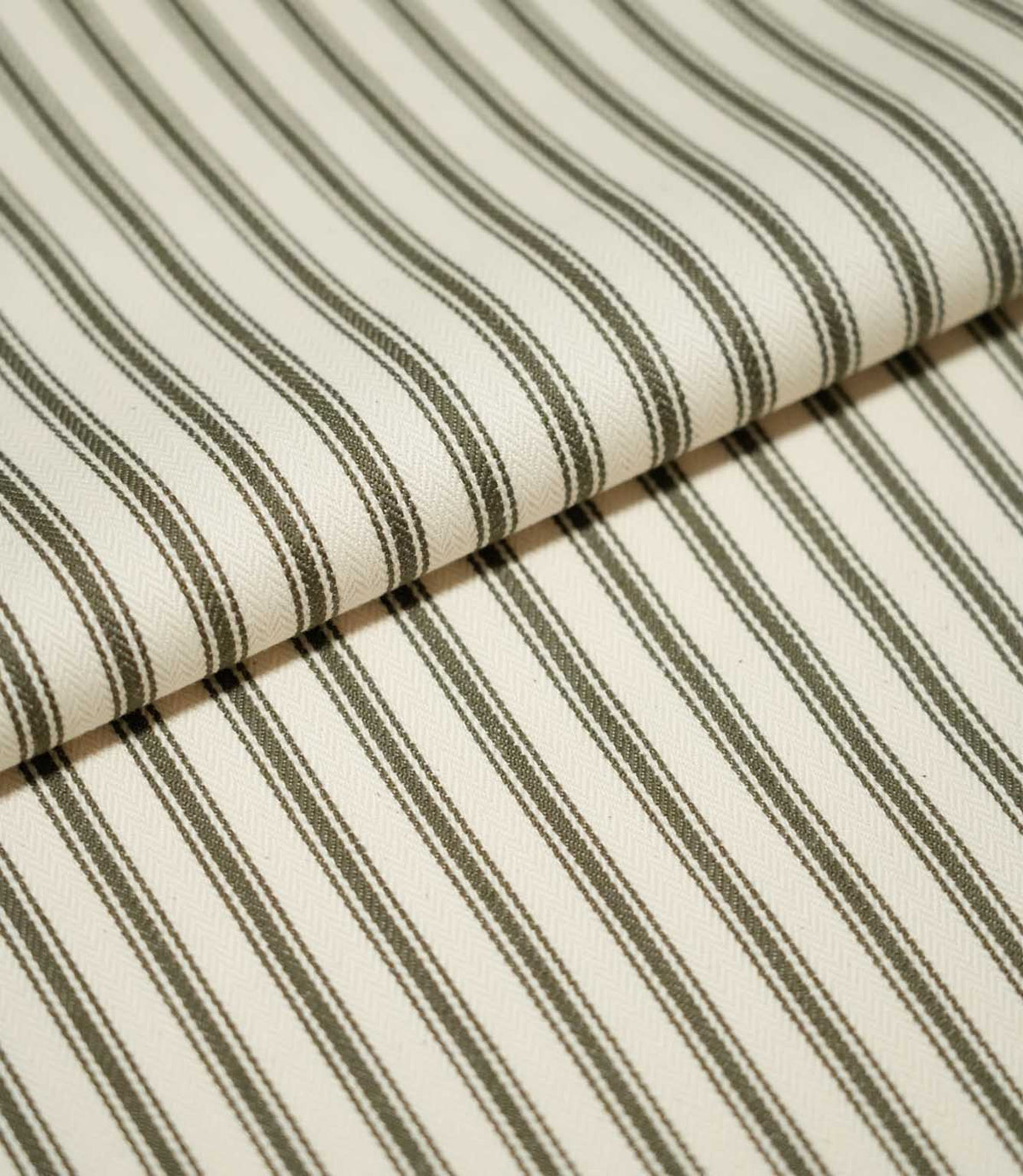 Folded JF Ticking Forest fabric showing its classic narrow forest green ticking stripe pattern on a warm ivory textured ground.