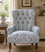 Floral patterned fabric armchair in a cosy country room with a lamp and books.