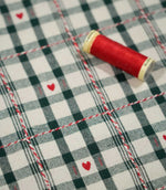 Cotswold Heart Tartan fabric with a red thread spool, highlighting the ivory and green checked design, small red hearts and textured woven detailing.