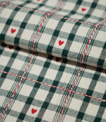 Folded Cotswold Heart Tartan fabric in ivory, green and red, showing the detailed check pattern, repeating heart motifs and woven texture.