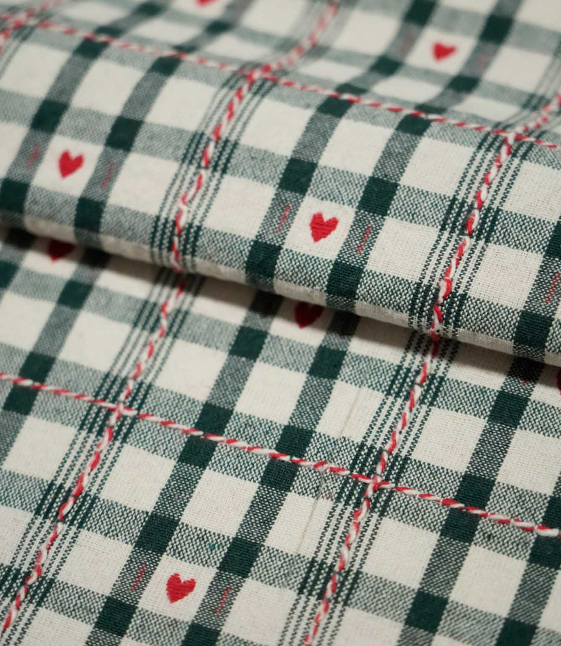 Folded Cotswold Heart Tartan fabric in ivory, green and red, showing the detailed check pattern, repeating heart motifs and woven texture.