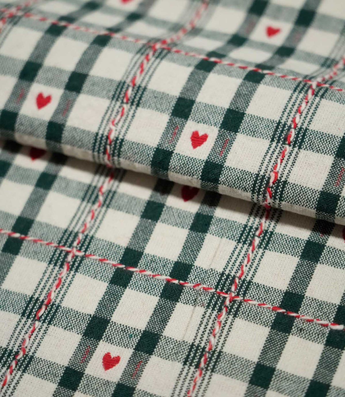Folded Cotswold Heart Tartan fabric in ivory, green and red, showing the detailed check pattern, repeating heart motifs and woven texture.