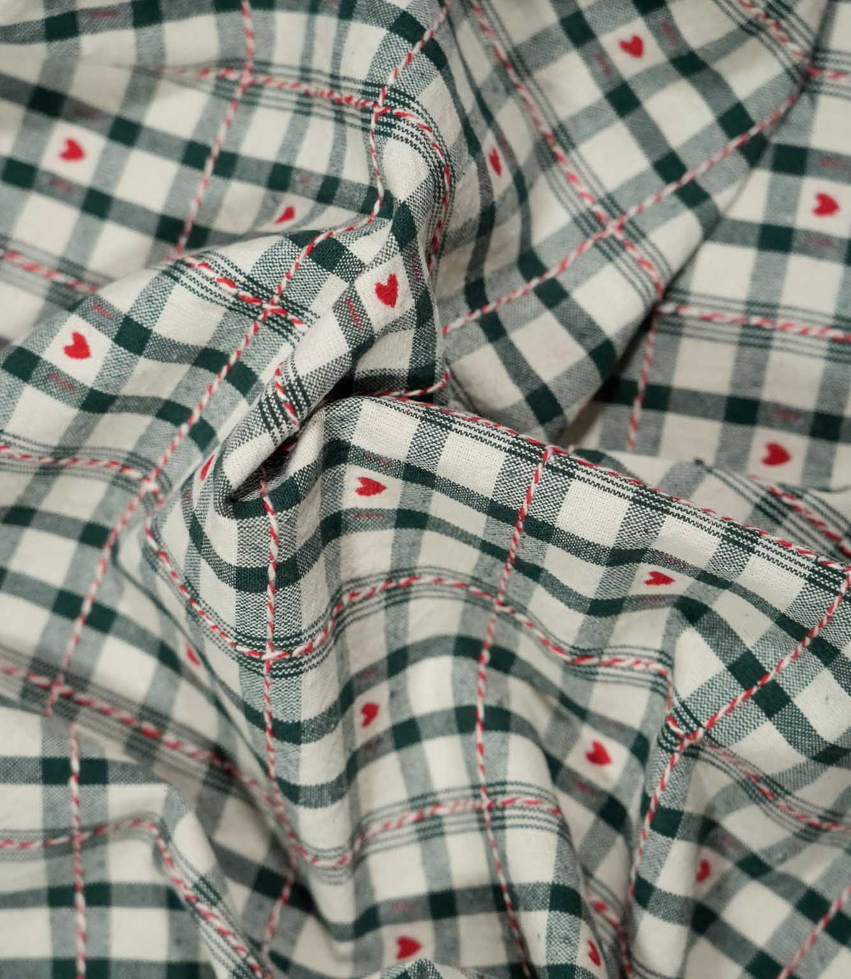 Draped Cotswold Heart Tartan fabric showing its soft handle and woven ivory and green check design with repeating red heart motifs.