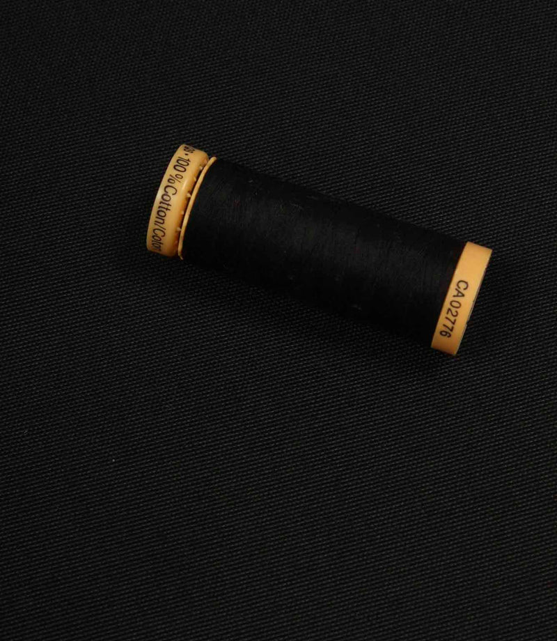 Black fabric with a matching Gütermann thread spool placed on top for colour comparison.