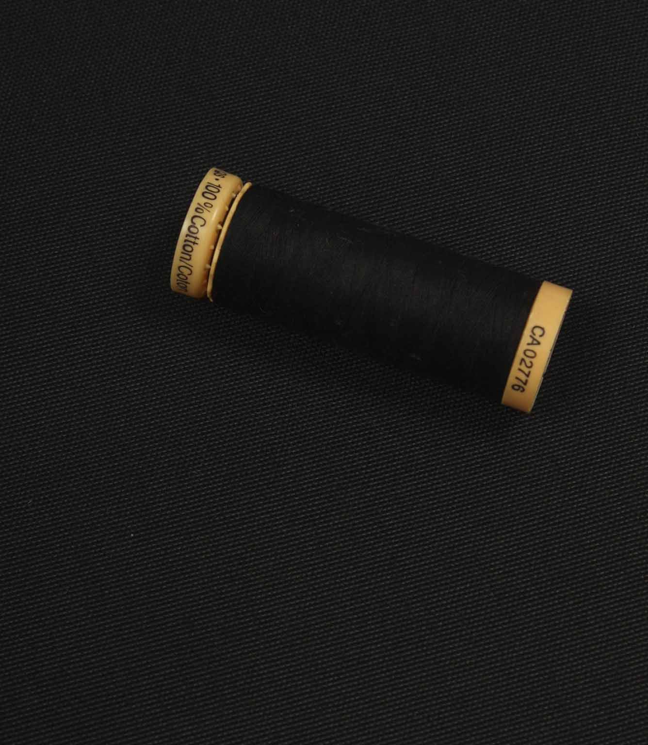 Black fabric with a matching Gütermann thread spool placed on top for colour comparison.