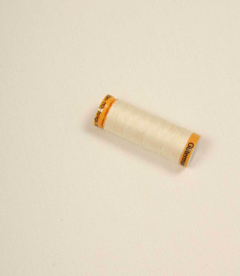 Cream fabric with a matching Gütermann thread spool placed on top for colour comparison.