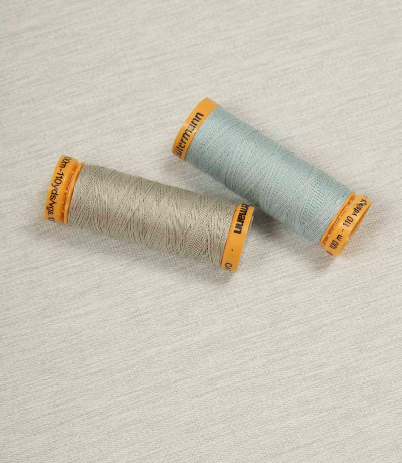 Grey fabric with coordinating Gütermann thread spools in neutral and pale blue for colour matching.