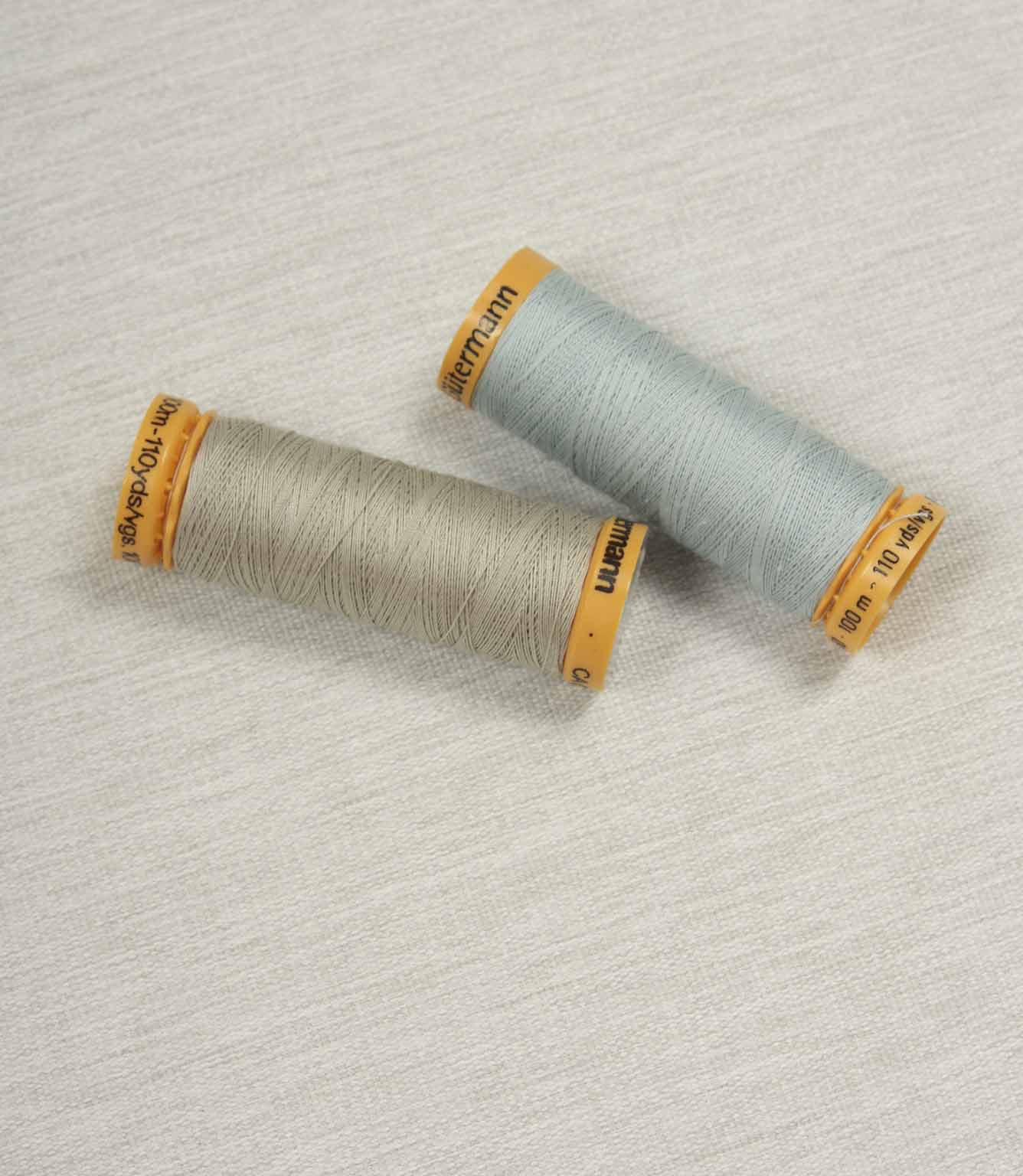 Grey fabric with coordinating Gütermann thread spools in neutral and pale blue for colour matching.