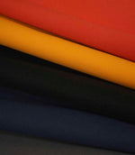 Layered plain weave fabric in red, mustard, black and navy, shown folded to highlight texture and colour contrast.