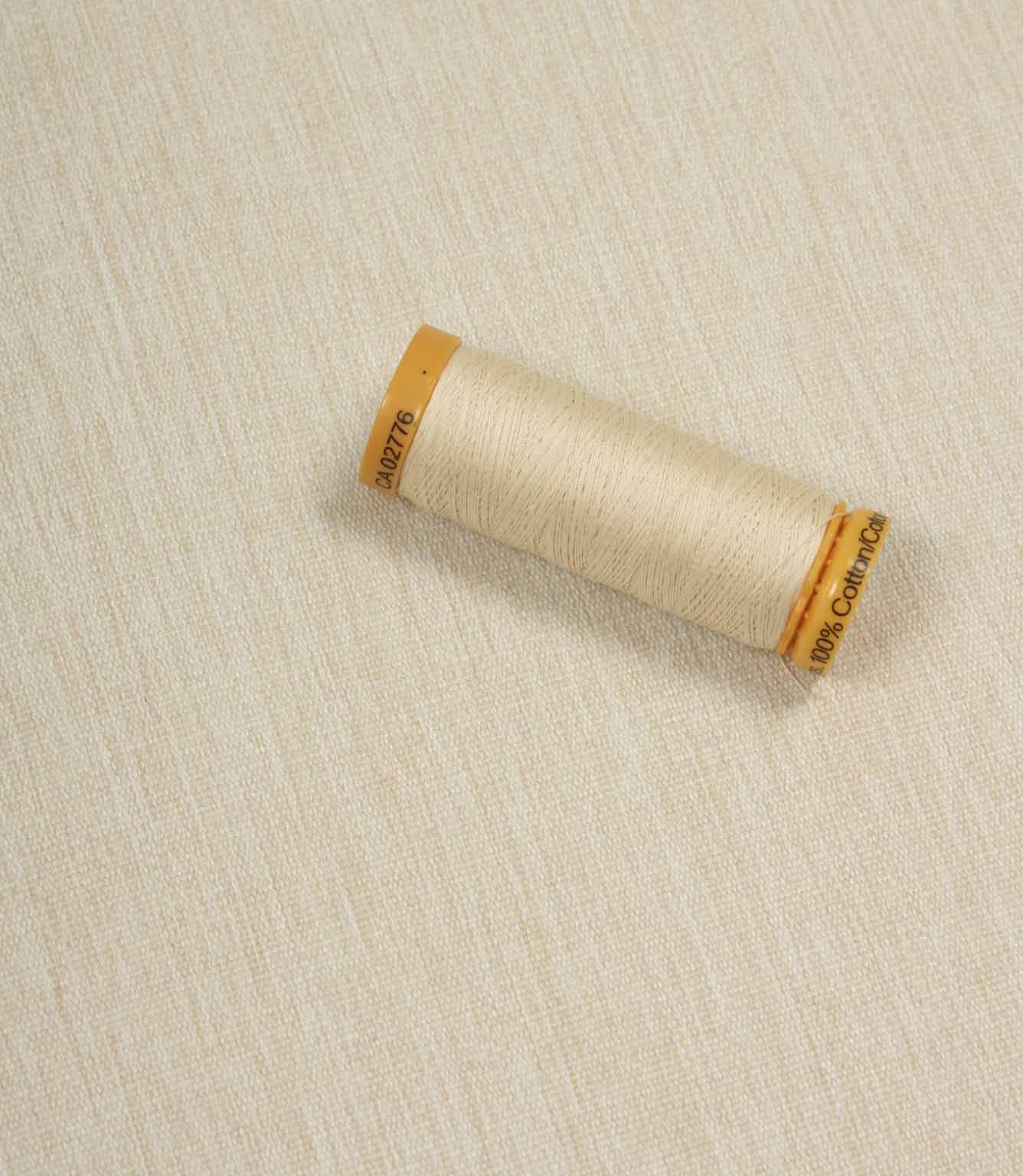Beige fabric with a matching Gütermann thread spool placed on top for colour comparison.