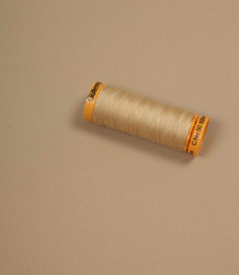 Beige fabric with a matching Gütermann thread spool placed on top for colour comparison.