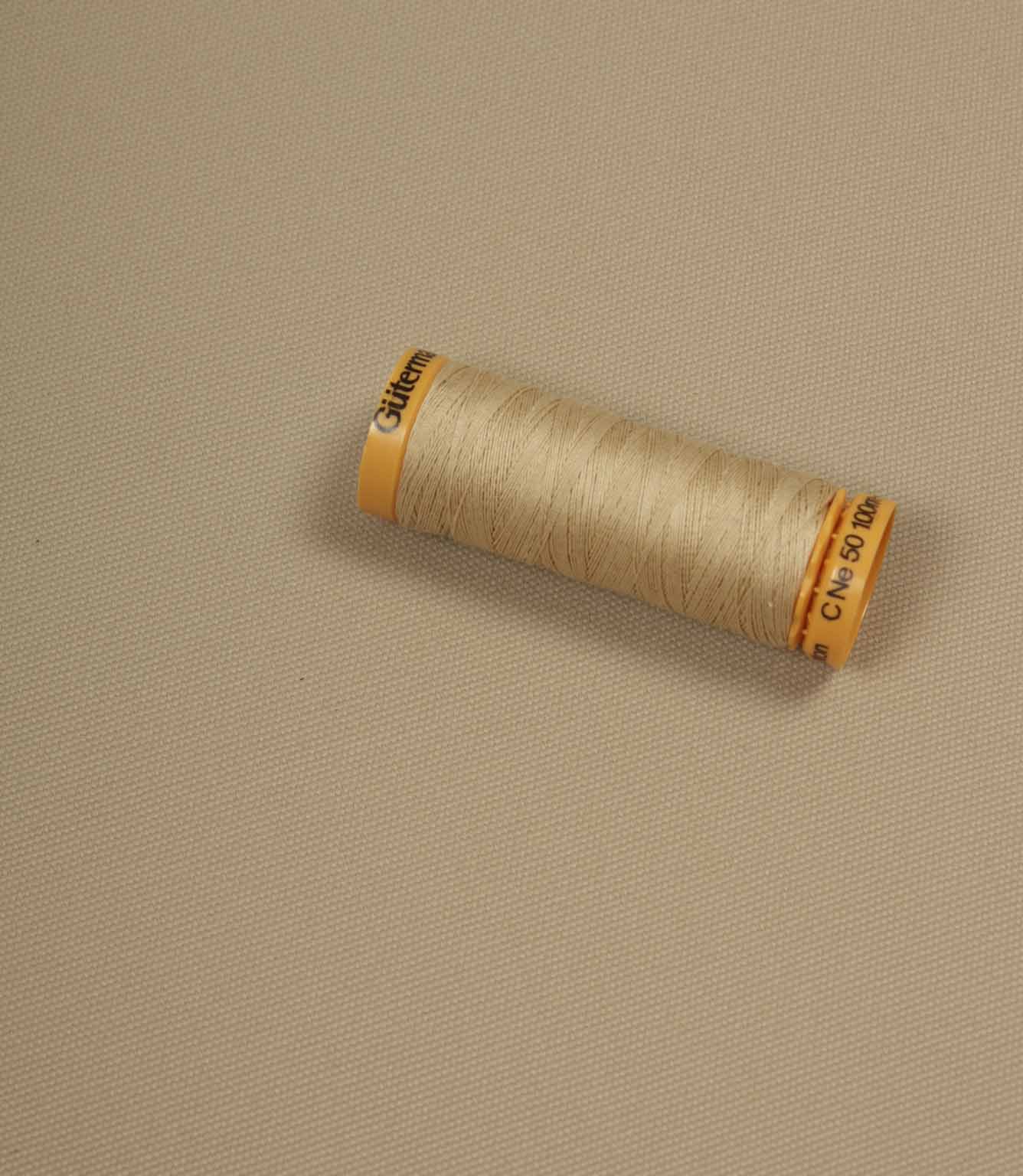 Beige fabric with a matching Gütermann thread spool placed on top for colour comparison.