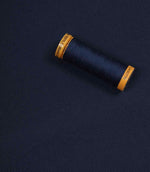 Navy blue fabric with a matching Gütermann thread spool placed on top for colour comparison.