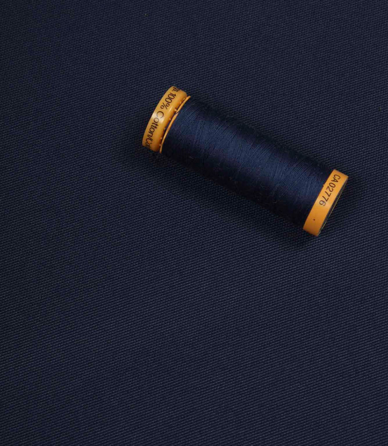 Navy blue fabric with a matching Gütermann thread spool placed on top for colour comparison.