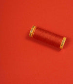 Orange fabric with a matching Gütermann thread spool placed on top for colour comparison.