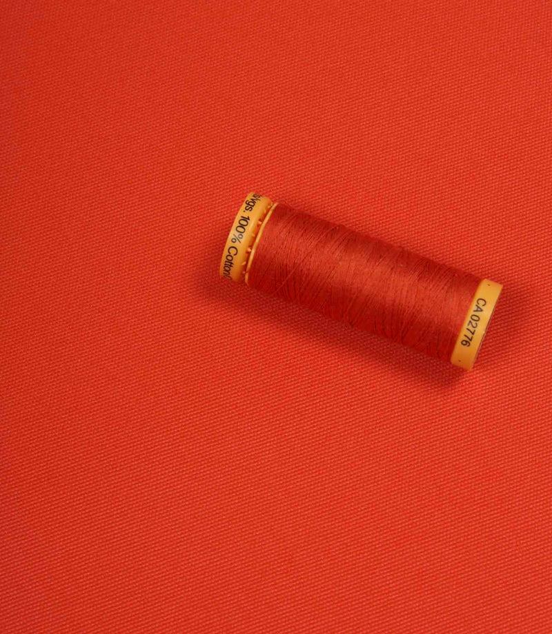 Orange fabric with a matching Gütermann thread spool placed on top for colour comparison.