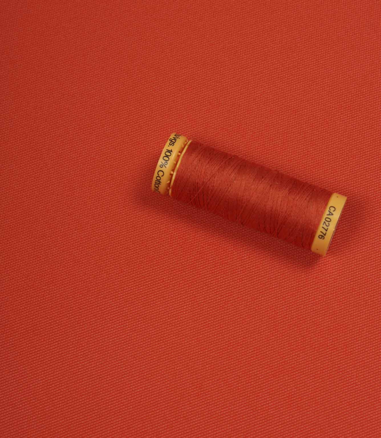 Orange fabric with a matching Gütermann thread spool placed on top for colour comparison.