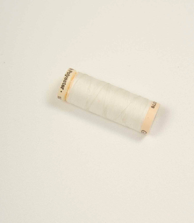 Ivory fabric with a matching pale thread spool placed on top for accurate colour comparison.