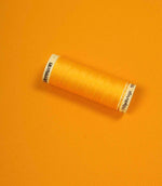Bright orange fabric with a matching Gütermann thread spool placed on top for colour comparison.