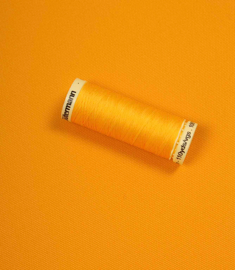 Bright orange fabric with a matching Gütermann thread spool placed on top for colour comparison.
