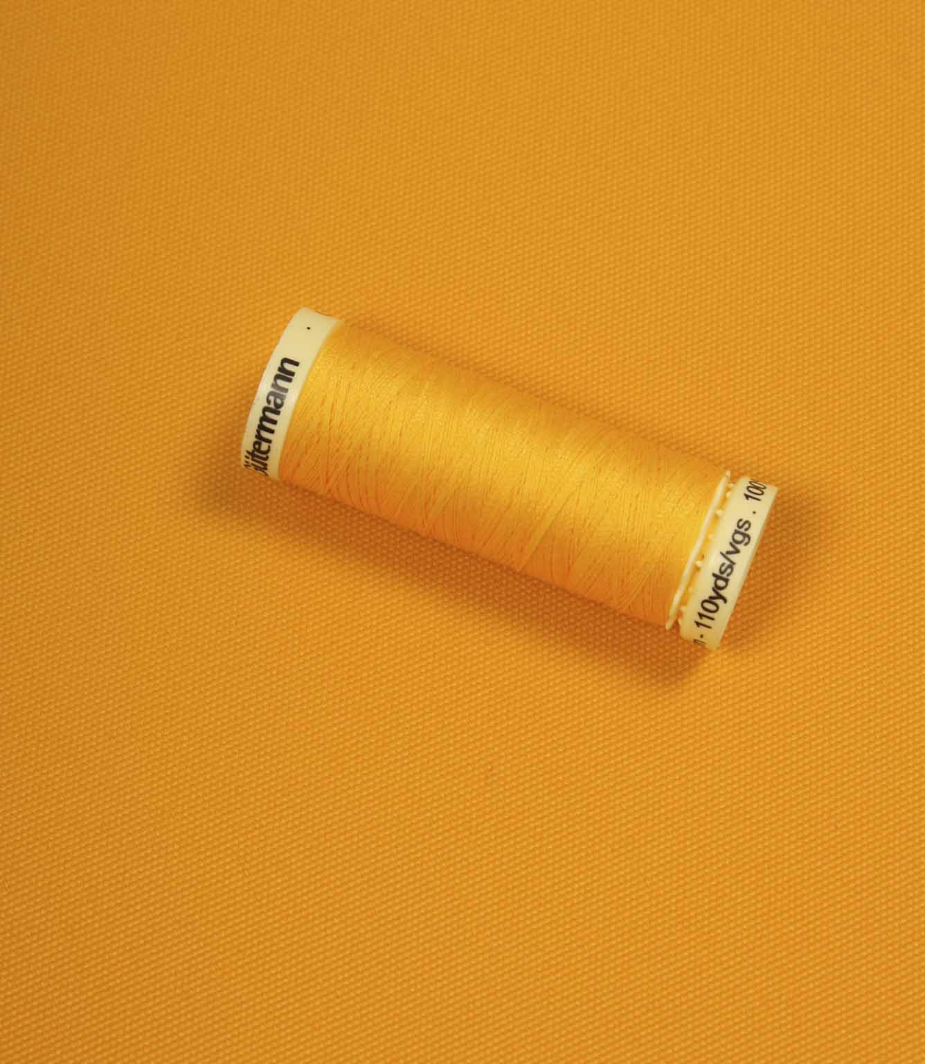 Bright orange fabric with a matching Gütermann thread spool placed on top for colour comparison.