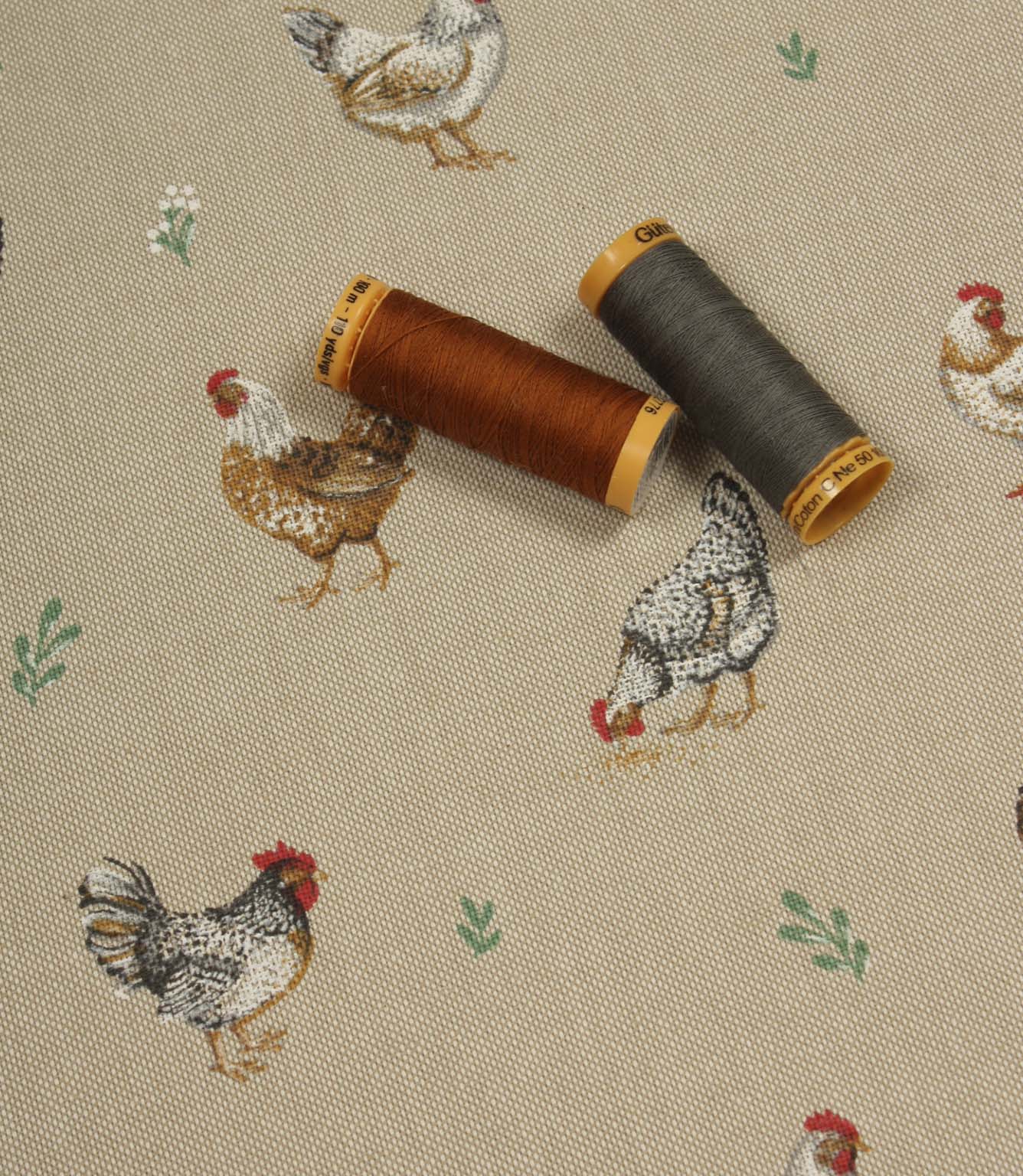 Farmhouse-inspired fabric with illustrated chickens on a neutral beige base, shown with coordinating rust and charcoal thread spools.