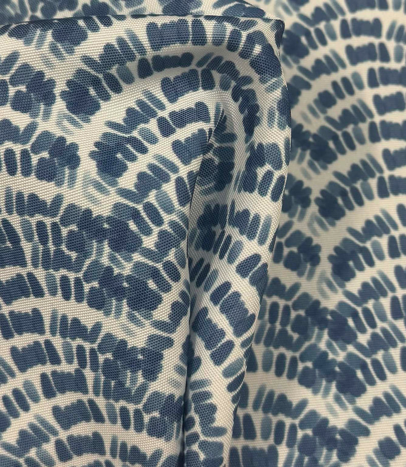 Draped coastal wave fabric showing flowing indigo blue geometric botanical shapes across a natural off-white background.