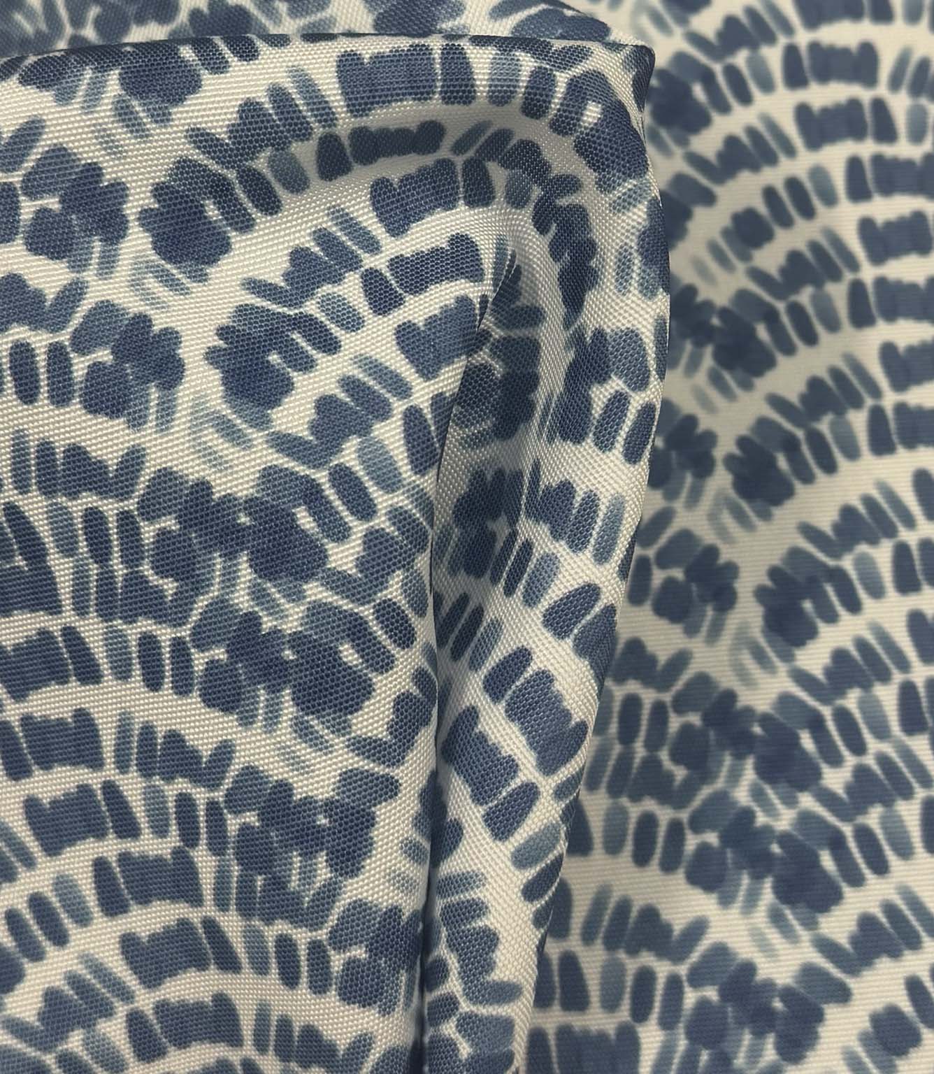 Draped coastal wave fabric showing flowing indigo blue geometric botanical shapes across a natural off-white background.